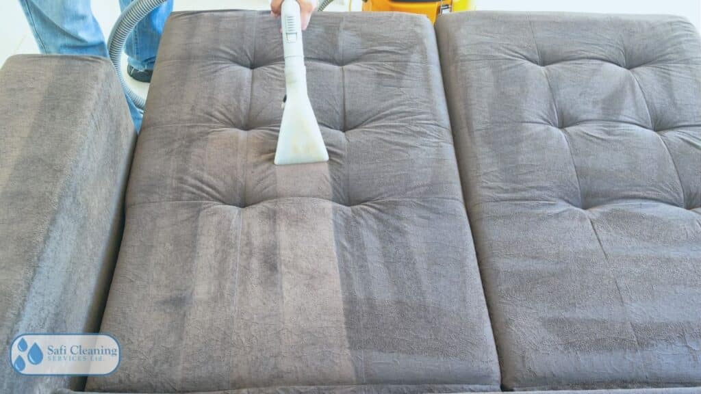Homeowner vacuuming an upholstered ottoman as part of regular furniture maintenance.